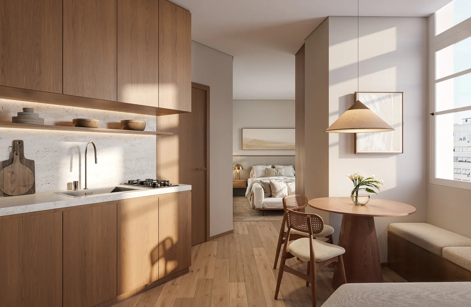 Studio com cozinha, mesa redonda e a cama ao fundo, junto à janela