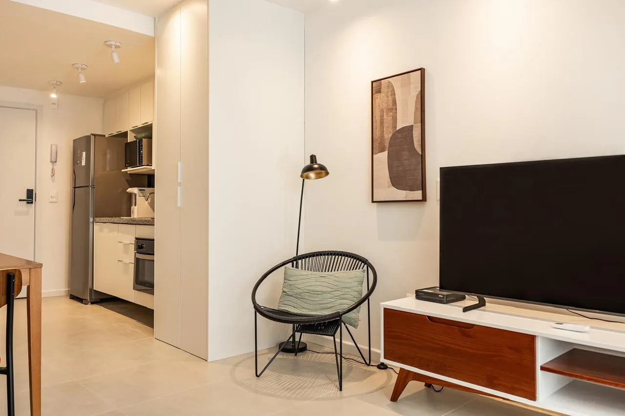 Foto real da sala de um studio decorado do Glória Del'Art, com TV e cozinha