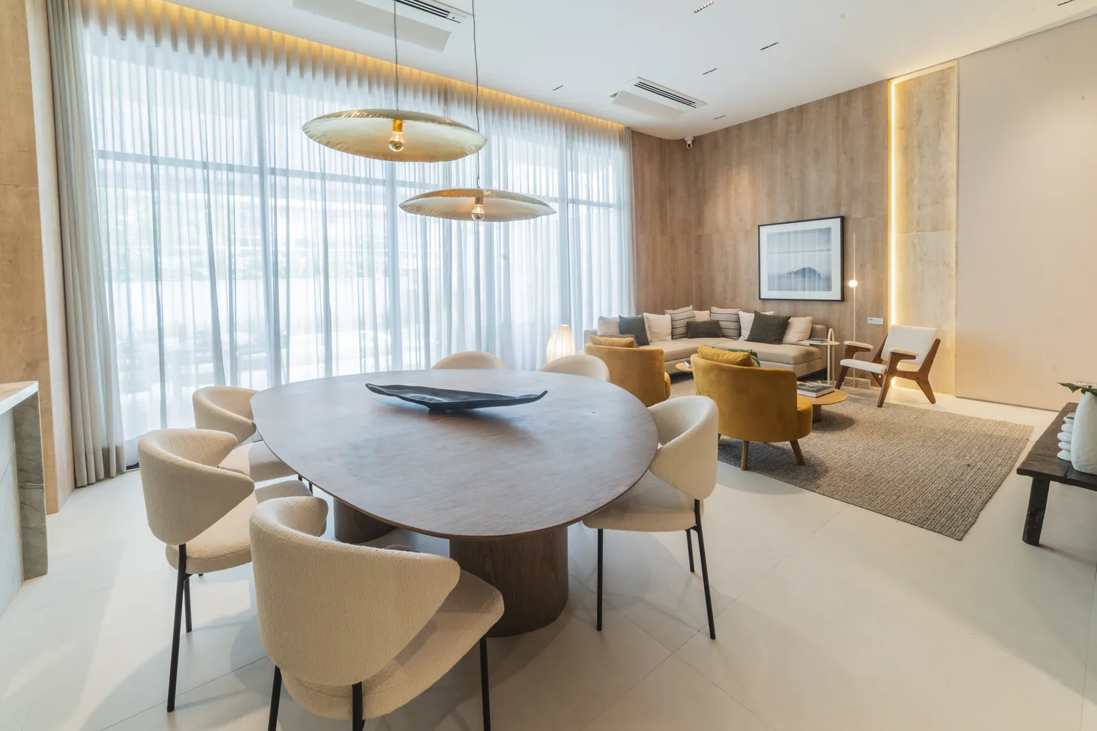 Mesa de jantar oval com luminária dourada e cortinas claras