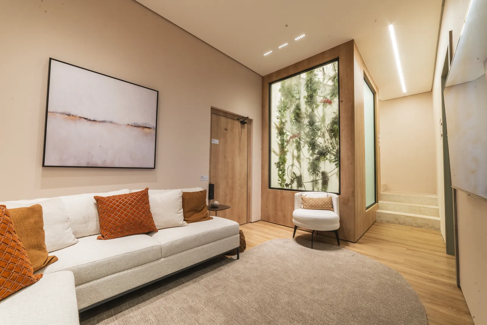 Sala íntima com sofá branco, almofadas laranja e jardim vertical