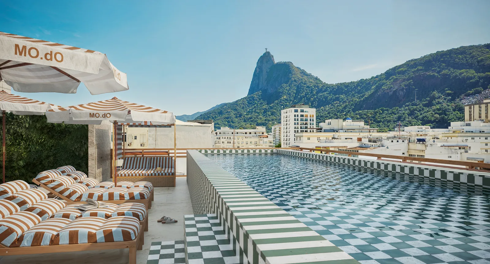 A piscina do rooftop com guarda-sóis e o Pão de Açúcar ao fundo