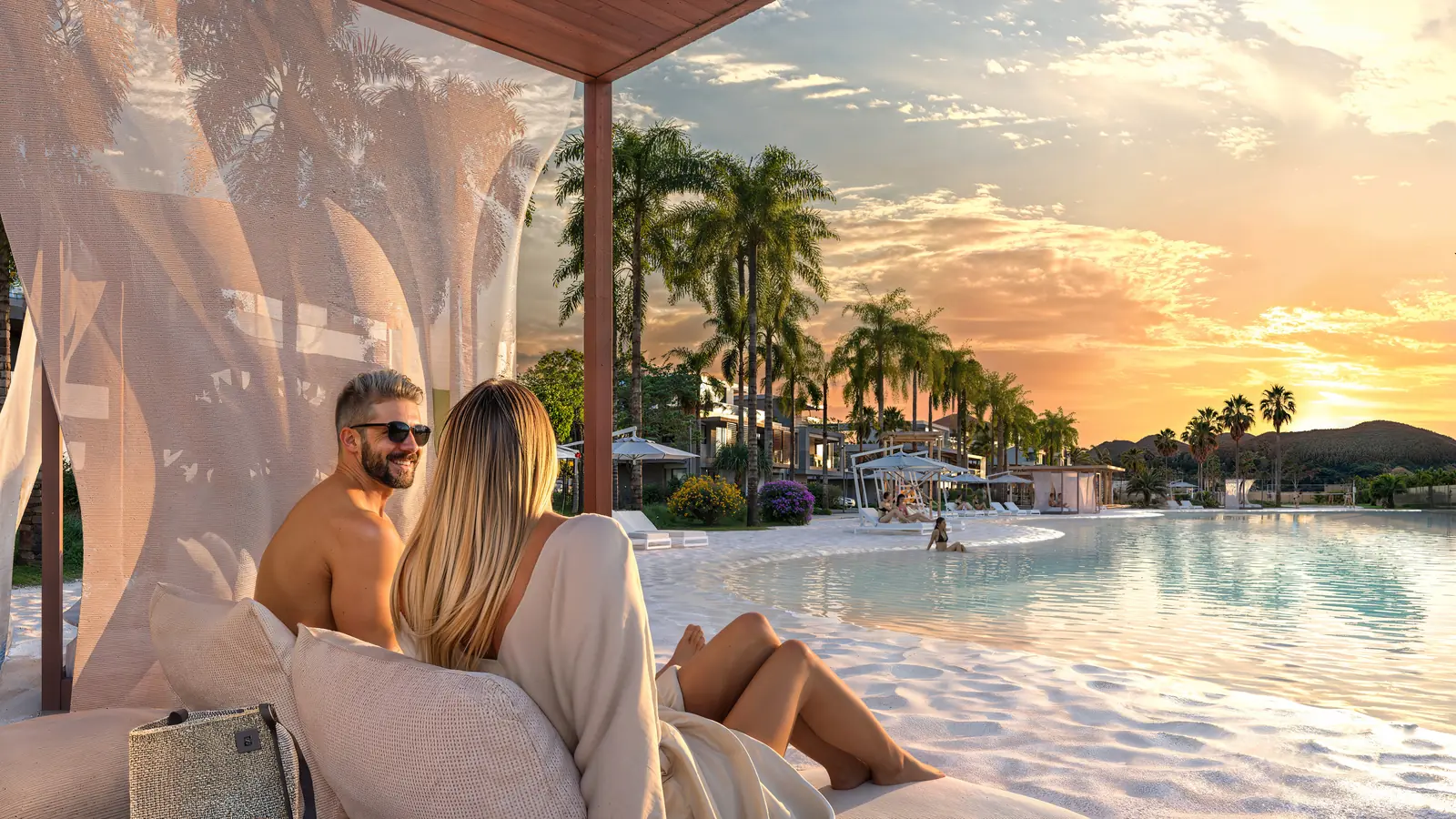Casal descansando num bangalô com cortinas brancas, ao pôr do sol