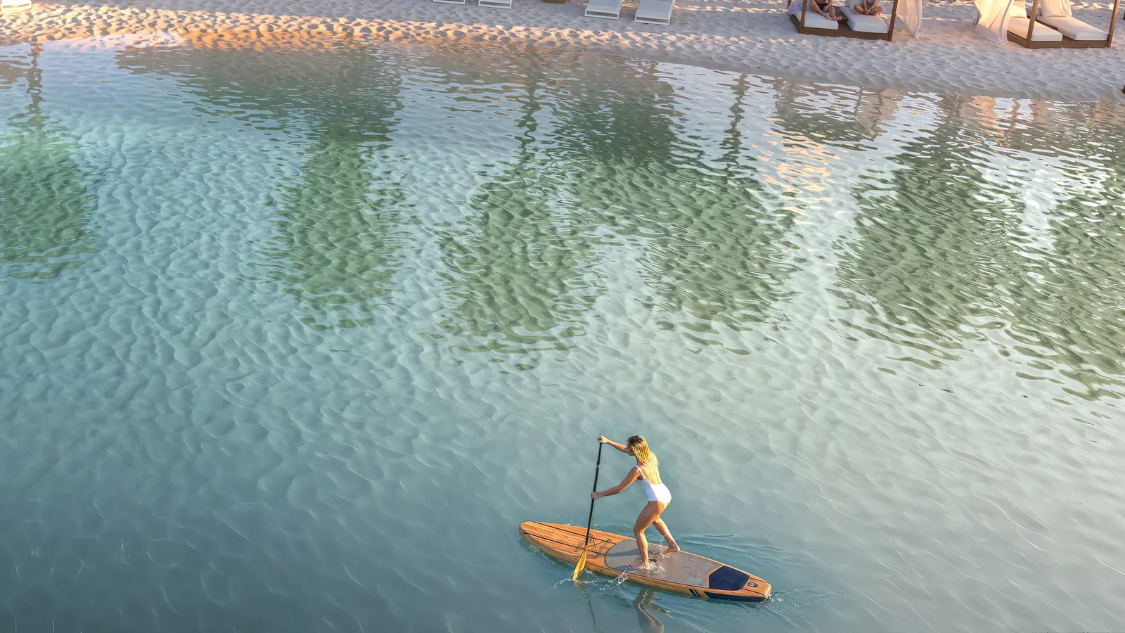Pessoa remando de stand-up paddle na água cristalina da prainha