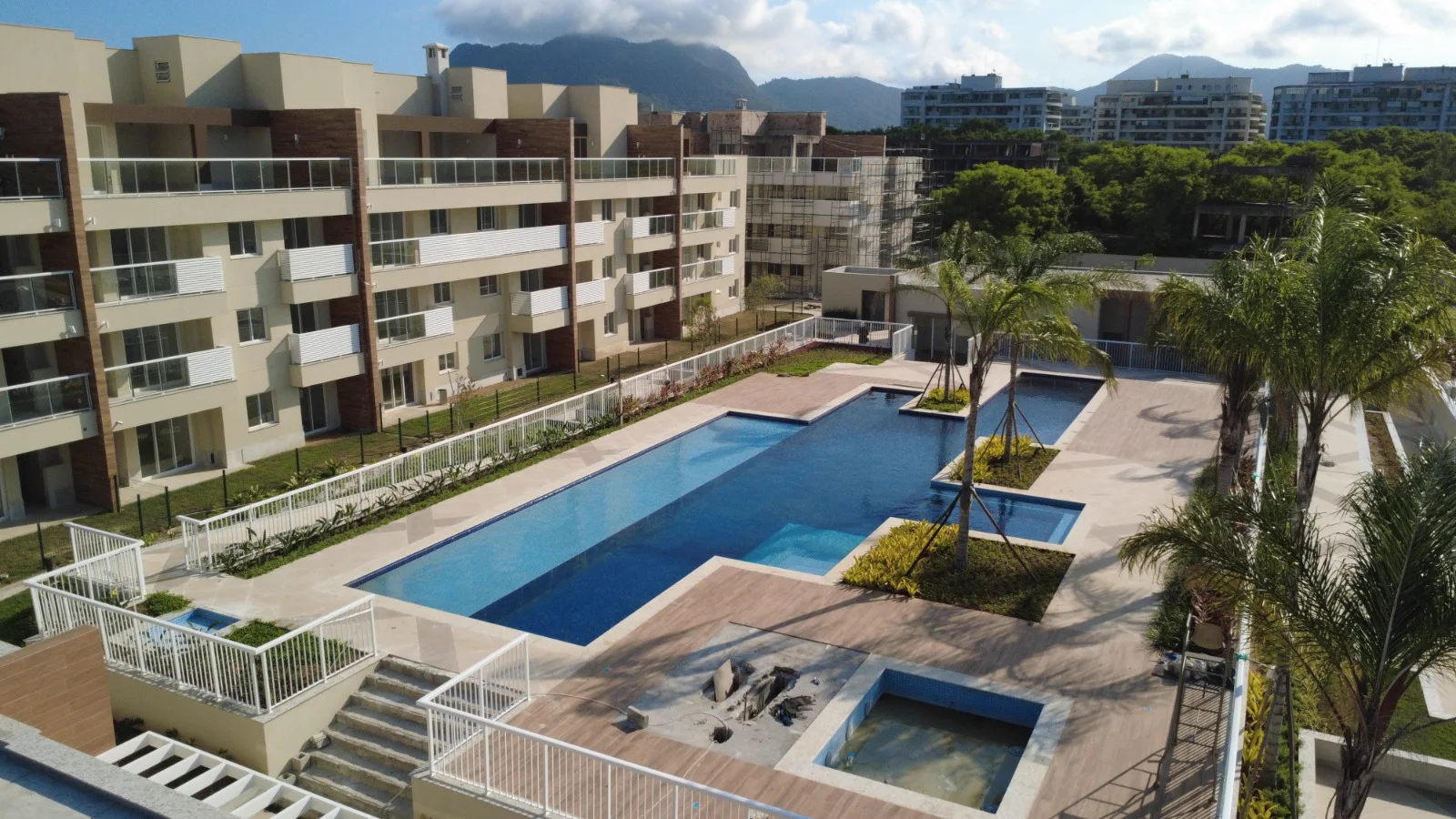 Foto real de drone da piscina do Clube Palms cheia, com o paisagismo pronto e os blocos ao lado