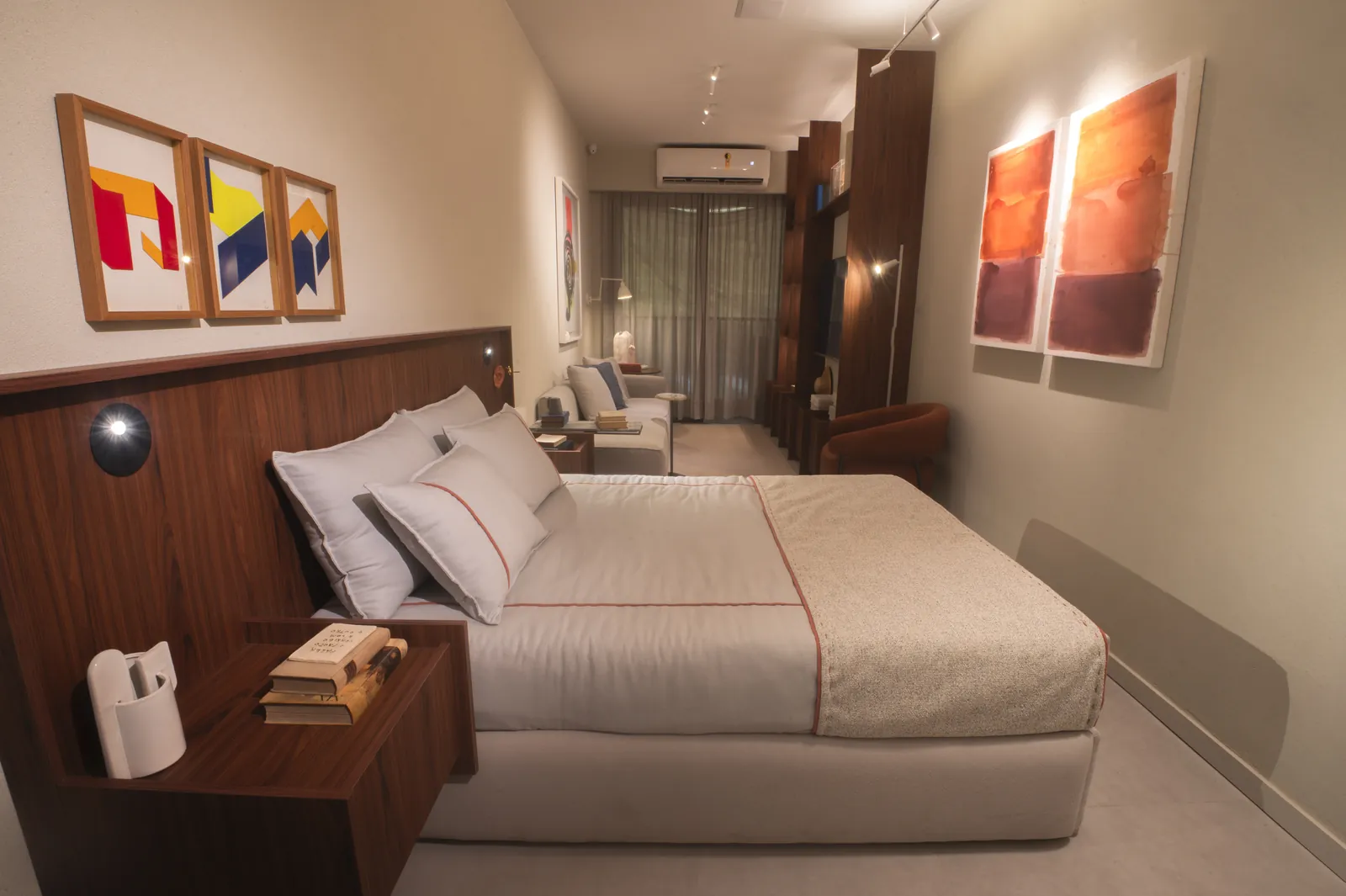 Studio decorado com cama de casal, cabeceira de madeira e quadros coloridos