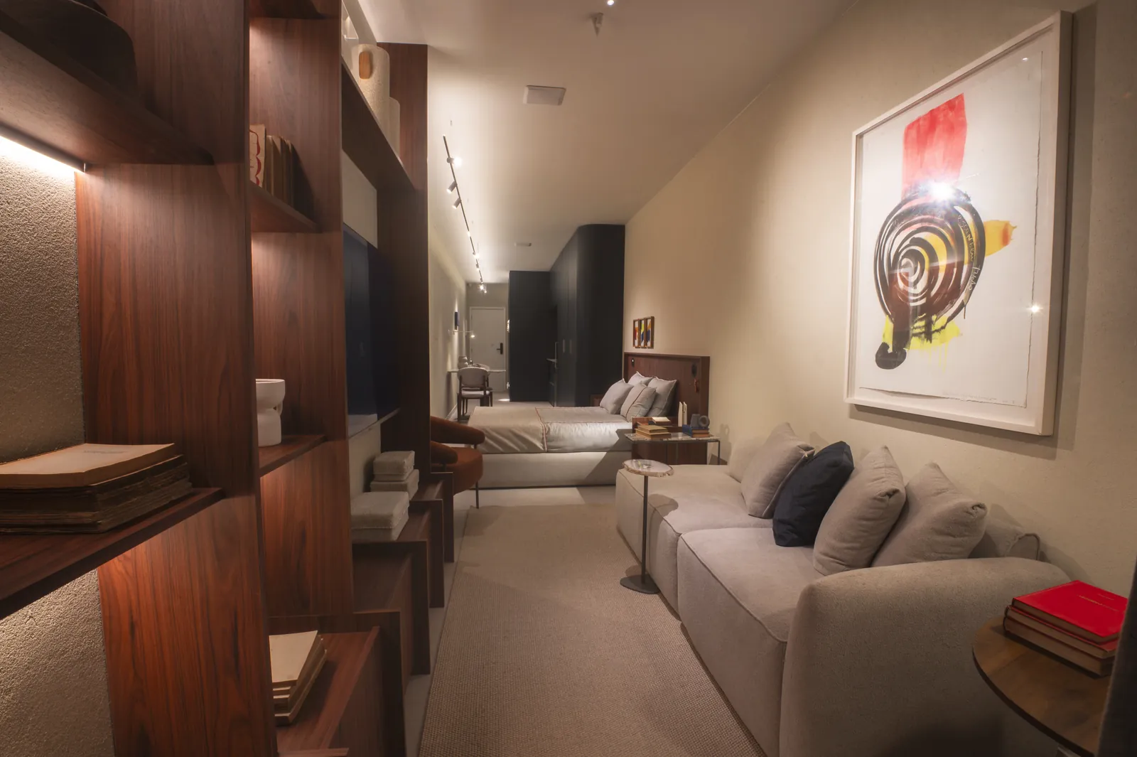 Estar do studio com sofá claro, estante de madeira e um quadro grande