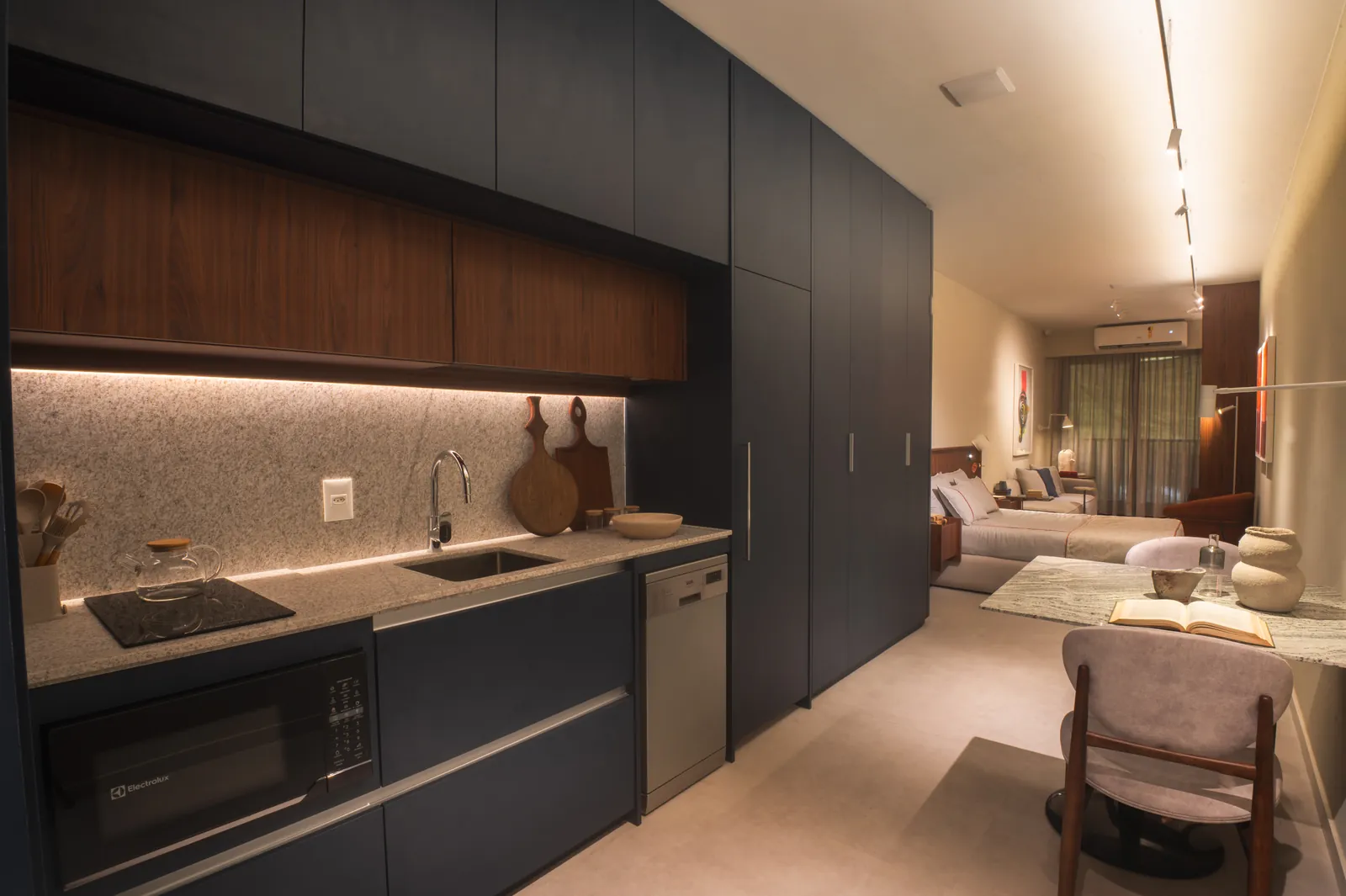 Cozinha escura com cooktop, micro-ondas e a cama ao fundo